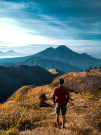 Rear view of man looking at mountains against sky