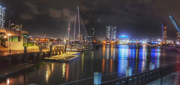 Illuminated city by river against sky at night