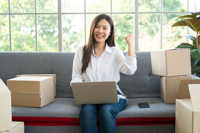 Portrait of smiling young woman using phone while sitting on sofa