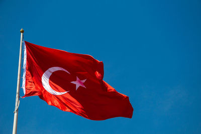 Low angle view of red flag against blue sky