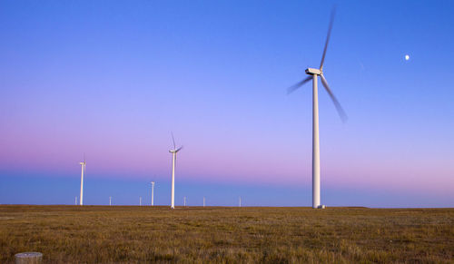Wind turbines in field against blue sky with moon