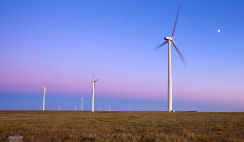 Wind turbines in field against blue sky with moon