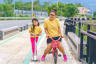 Little child girl to ride scooter with mother ride on small bicycle outdoor sports 