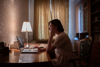 Female student thinking and using laptop