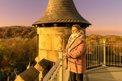 Side view of woman looking away while standing by railing at sunset