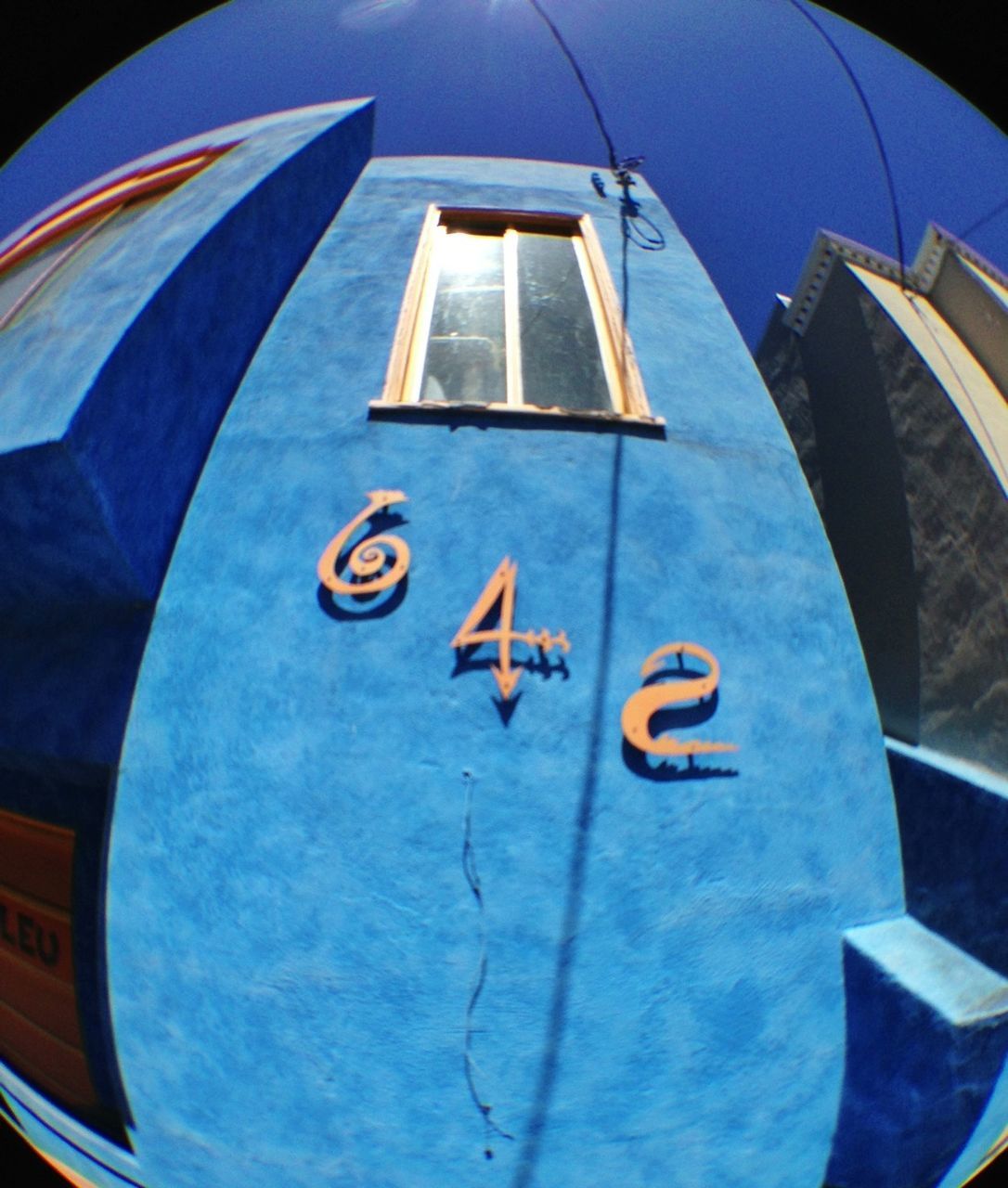 low angle view, blue, built structure, architecture, window, sky, building exterior, flying, transportation, day, mode of transport, part of, no people, airplane, sunlight, outdoors, building, multi colored, mid-air, air vehicle