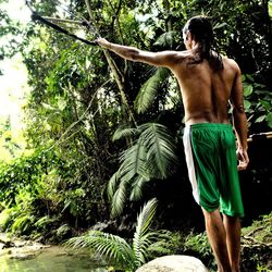 Rear view of shirtless man standing against trees