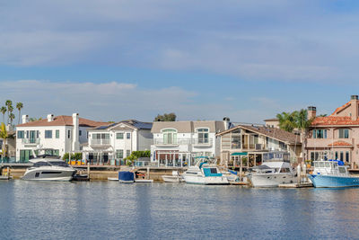 Boats moored at harbor by buildings in city against sky