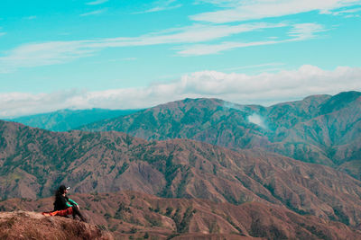 Woman sitting on mountain against sky