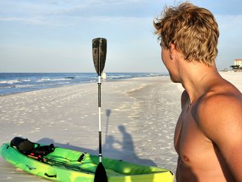 Young man from behind ready to kayak on the beach.