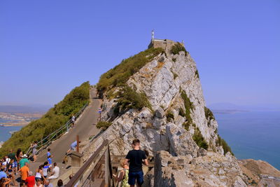 People on mountain by sea against clear sky