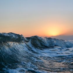 Waves curling in sea against clear sky during sunset