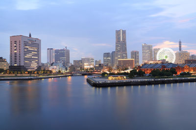 Illuminated buildings by river against sky in city