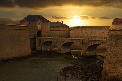 Arch bridge over river against buildings during sunset