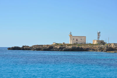 Lighthouse by sea against clear blue sky