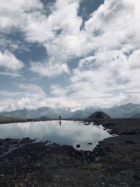 Distant view of man walking by lake against sky