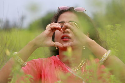 Close-up of young woman making heart shape on field