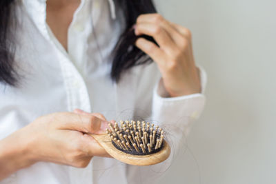 Midsection of woman holding hairbrush against wall