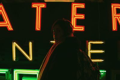 Portrait of woman standing by illuminated text at night