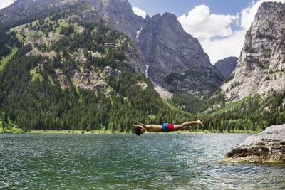 Teenager diving into lake by mountains