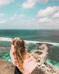 Rear view of woman with hand in hair standing against sea