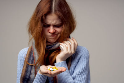 Young woman making face while holding medicines against gray background