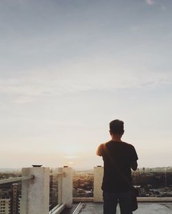 Rear view of man standing on retaining wall against sky