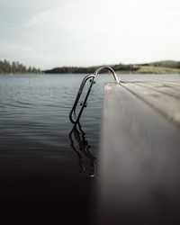 Ladder on wooden pier by lake against sky