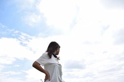 Low angle view of woman standing with hand on hip against cloudy sky