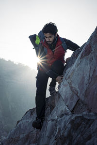 Young indian climber and traveler climbing up the mountain rock during sunset. adventure and sports
