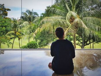 Rear view of woman standing by palm trees against sky