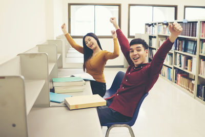 Portrait of cheerful friends with arms raised studying in library
