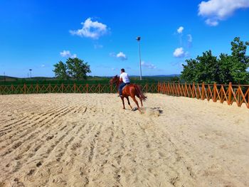 Man riding horse on ranch against sky