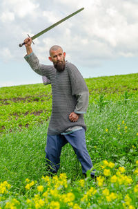 Emotional photo of medieval viking in metal chain mail swinging sword. background of green grass