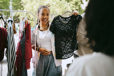 Excited female customer holding dress while talking to merchant at flea market