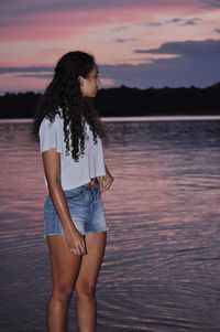 Beautiful woman standing by lake against sky during sunset