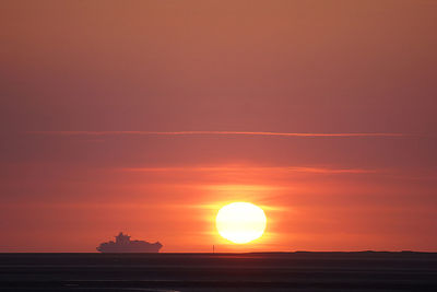 Mid distance view of silhouette container ship in sea against sky during sunset