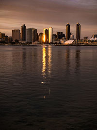 Sea by illuminated buildings against sky during sunset