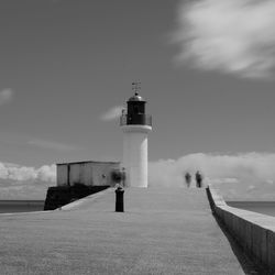 Lighthouse on footpath by sea against sky