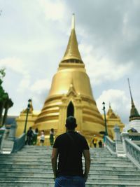 Rear view of man standing in front of wat phra kaew against sky