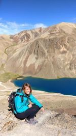 High angle view of smiling young woman sitting on rock against mountains