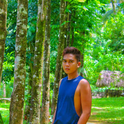 Portrait of young man standing by trees on field