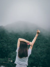 Rear view of woman with arms raised standing in fog
