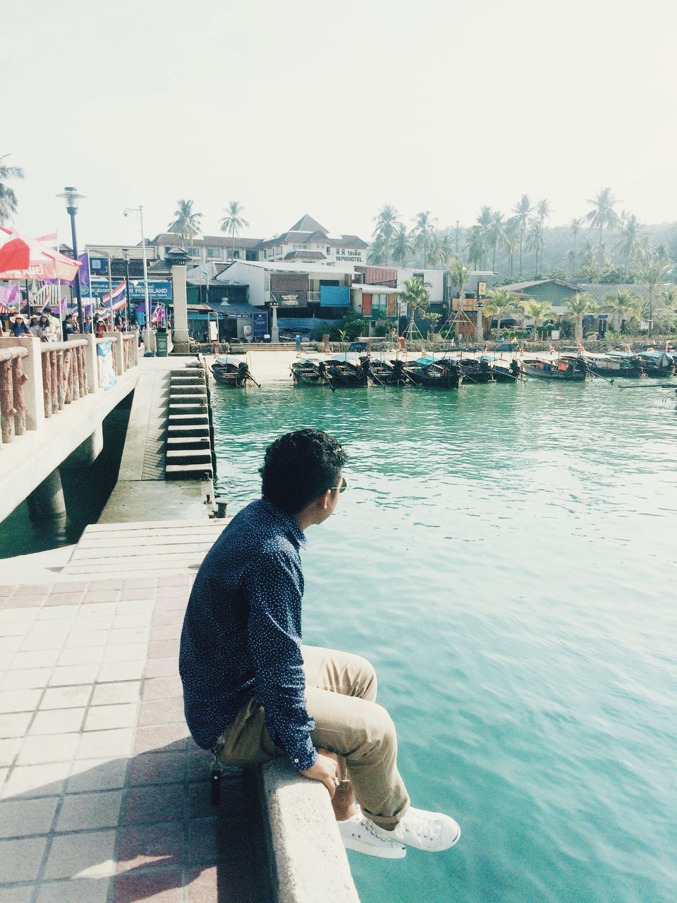 water, rear view, lifestyles, leisure activity, men, clear sky, person, pier, built structure, casual clothing, standing, railing, full length, sea, sitting, river, architecture, day