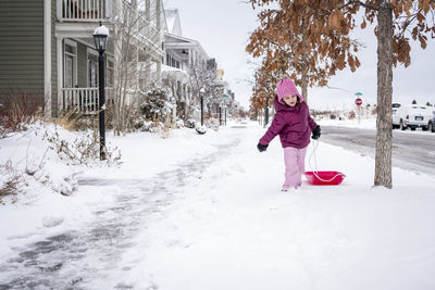 Cute girl pulling sled while walking on snow covered road