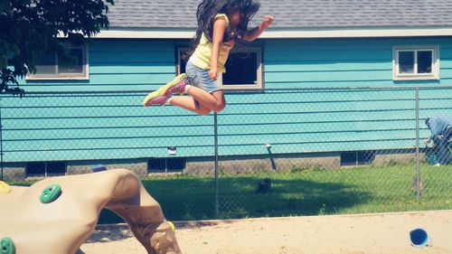 Side view of girl jumping at playground against house