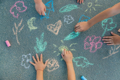 Hands of girls and boy drawing with chalk on footpath