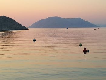 Buoys floating in sea by mountain against clear sky during sunset