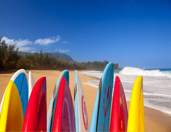 Close-up of multi colored umbrellas on beach against blue sky