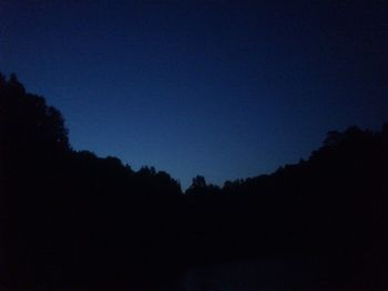 Silhouette trees against clear blue sky at night